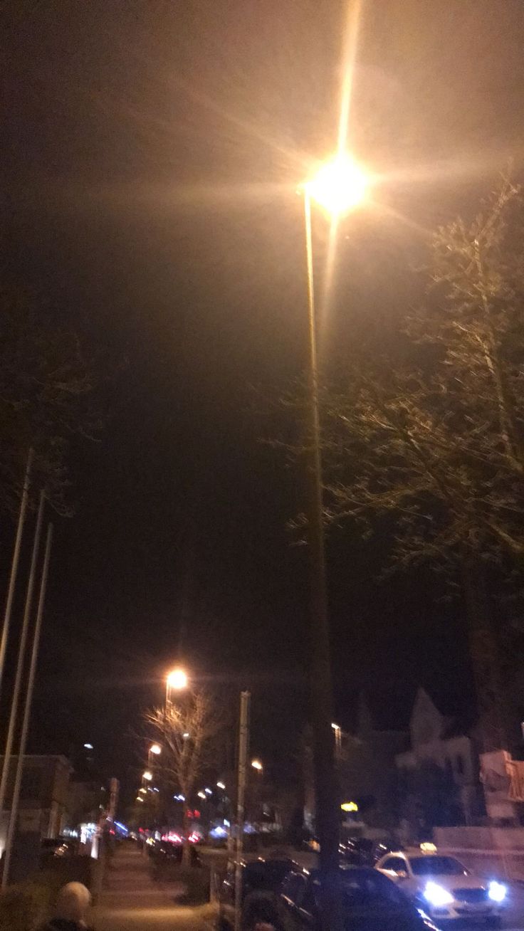 an empty street at night with cars parked on the side walk and people walking down the sidewalk