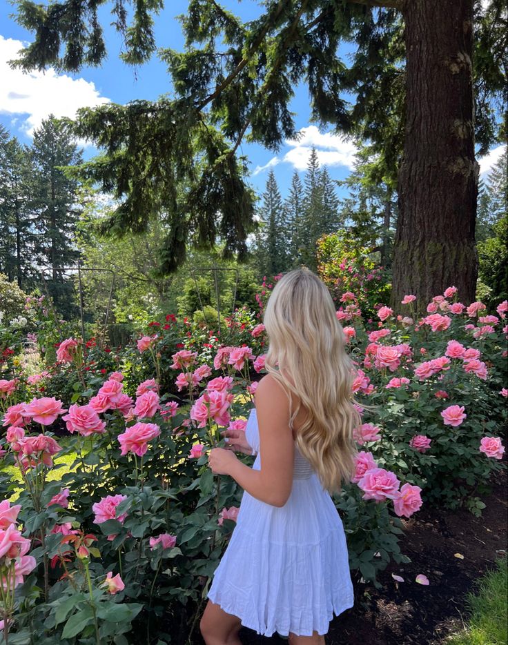 a blonde woman standing in front of pink flowers with her back turned to the camera