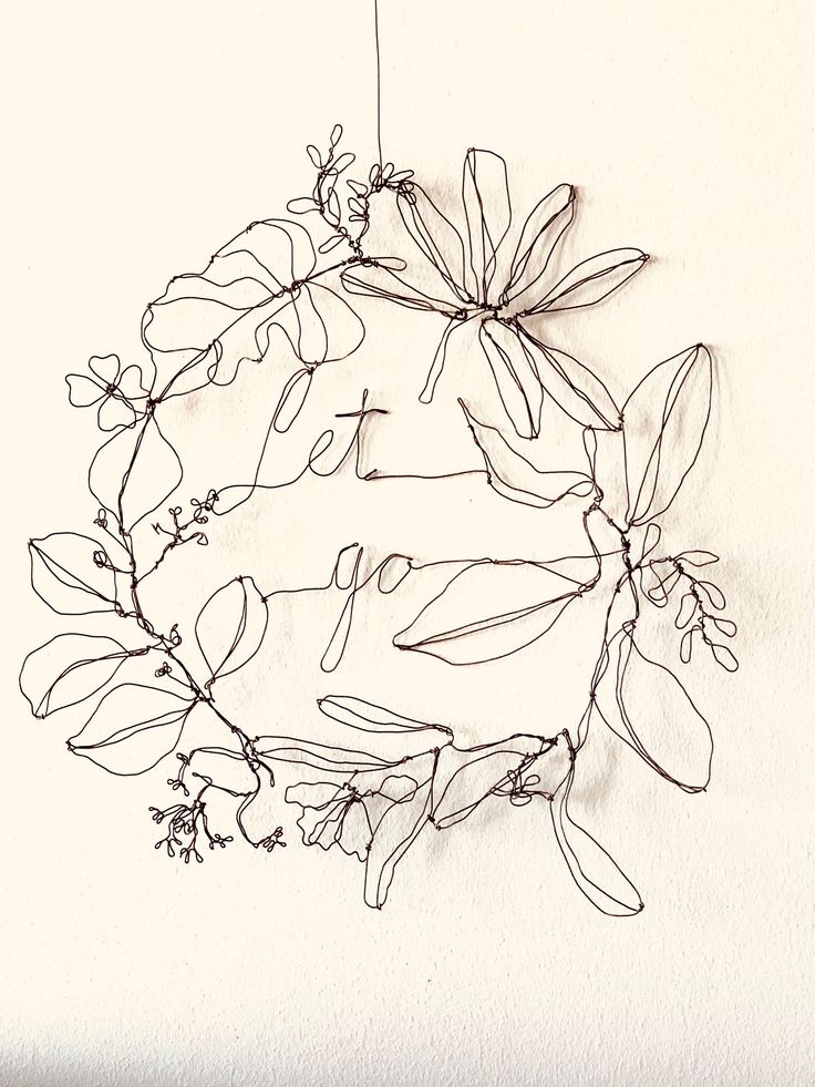 a wire wreath with flowers hanging from it's sides on a white wall next to a pen and ink drawing