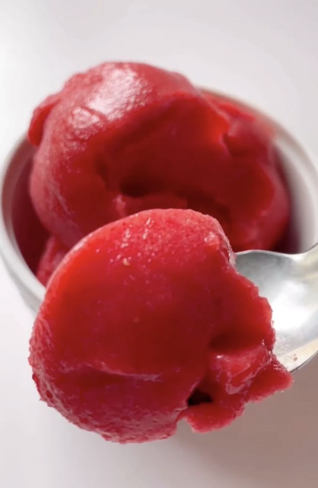 two scoops of red ice cream in a white bowl with a spoon next to it