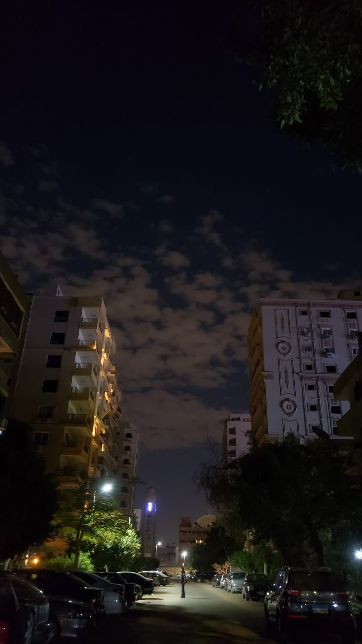 cars parked on the side of a street at night with tall buildings in the background