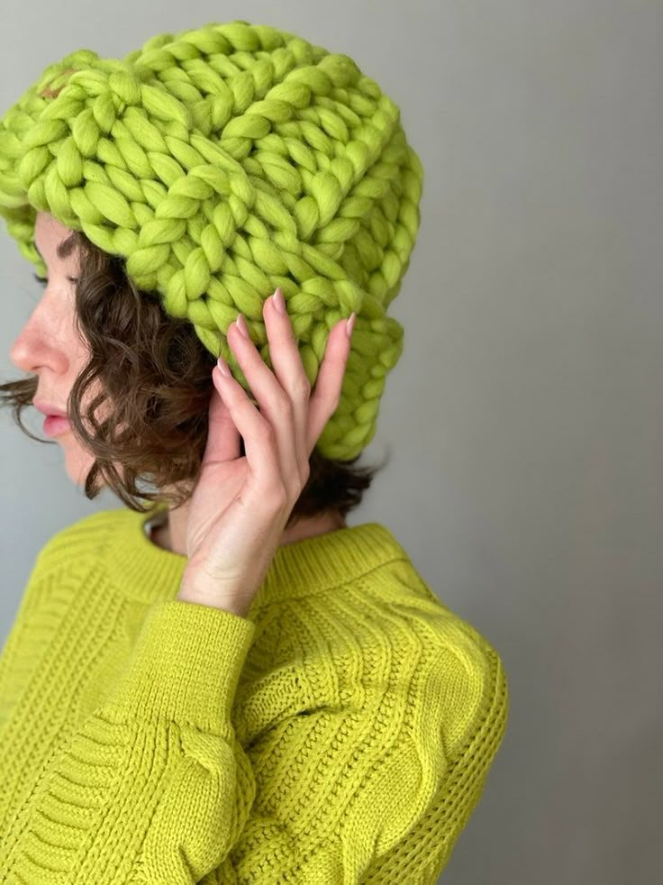 a woman wearing a green knitted hat and holding her hands up to her face