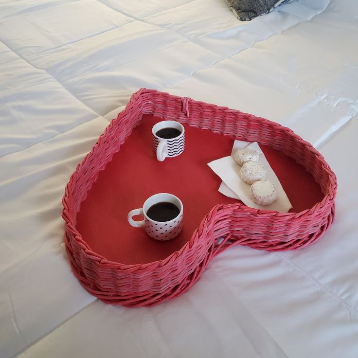 a wicker tray with two cups of coffee and pastries in it on a bed