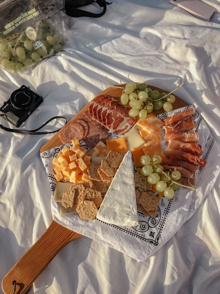 an assortment of cheeses, crackers and meats on a platter with a camera in the background