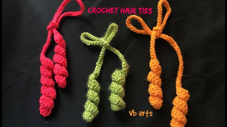 three crochet hair ties are lined up on a black surface, one is orange and the other is green