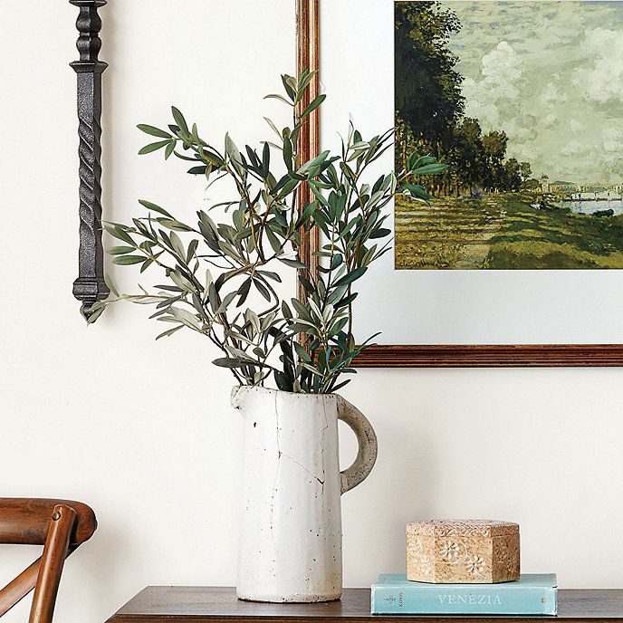 a vase filled with green plants sitting on top of a wooden table