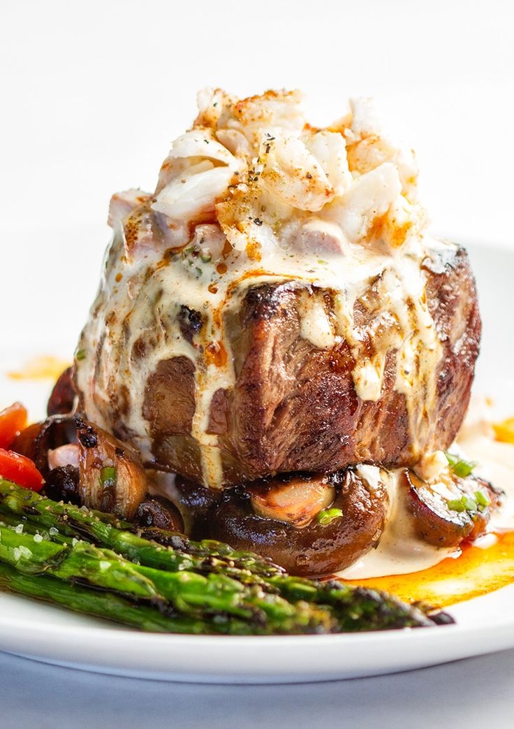 a white plate topped with steak and asparagus on top of a bed of sauce