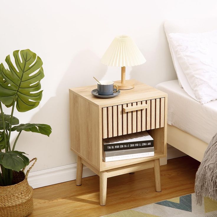 a nightstand with a lamp on it next to a bed and a potted plant