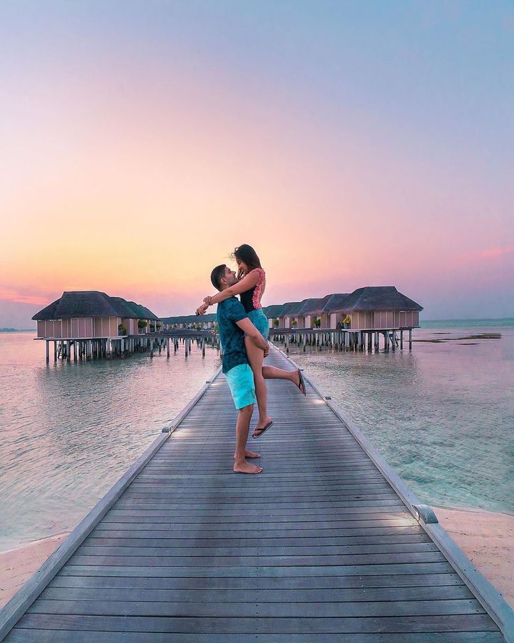 a man and woman are kissing on a pier over the water at sunset or sunrise