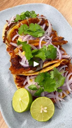 three tacos on a plate with limes and cilantro