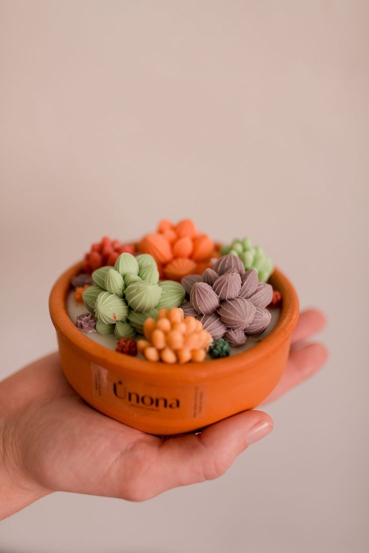 a hand holding a small orange bowl filled with tiny colorful flowers on top of it