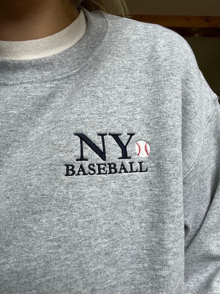 This NY Baseball embroidered sweatshirt is perfect for all the baseball lovers out there! This design is a bit smaller and placed to the left chest, we think it's super cute with the little baseball embroidered next to the words in navy threads! The sweatshirt color is our sport gray color and the brand of sweatshirt is Gildan. It's a unisex sweatshirt that's 50% cotton so it may shrink a little in the dryer! We find the sweatshirts to be true to size. Each sweatshirt has a permanent inner layer Crew Neck T-shirt With Letter Embroidery For College, Navy Top With Embroidered Logo For College, Embroidered Logo Tops For College Style Streetwear, Streetwear Tops With Embroidered Logo, Varsity Crew Neck Tops With Embroidered Graphics, Game Day T-shirt With Embroidered Logo, Sporty T-shirt With Embroidered Logo For Game Day, Collegiate Streetwear Sweatshirt For Baseball Season, Custom Embroidered Tops For Streetwear