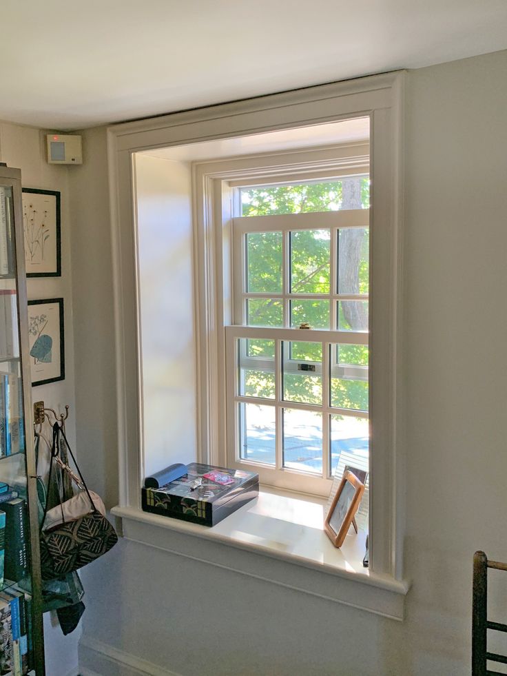 an open window in a white room with pictures on the wall and a book shelf