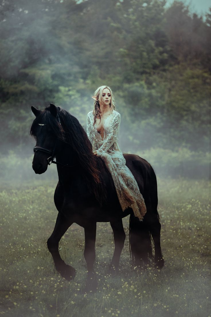 a woman riding on the back of a black horse in a field filled with grass