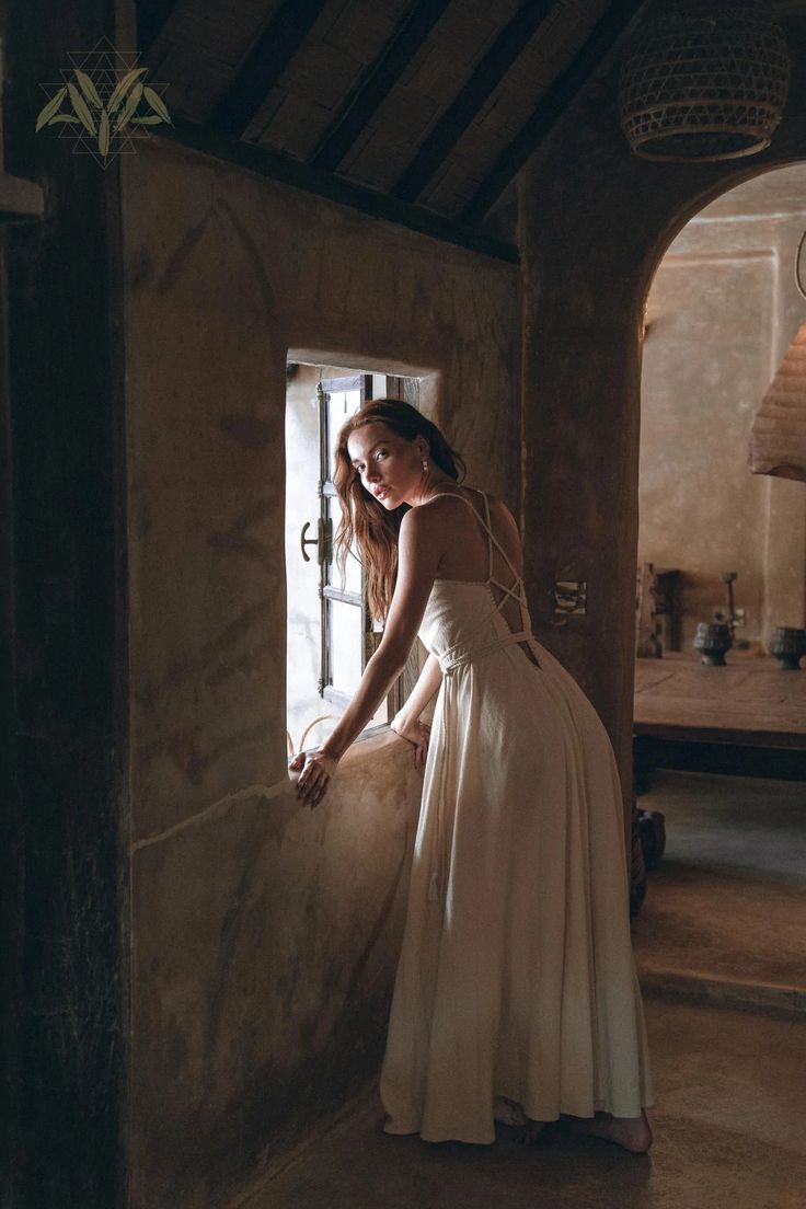 a woman in a white dress leaning against a wall with her hand on the door