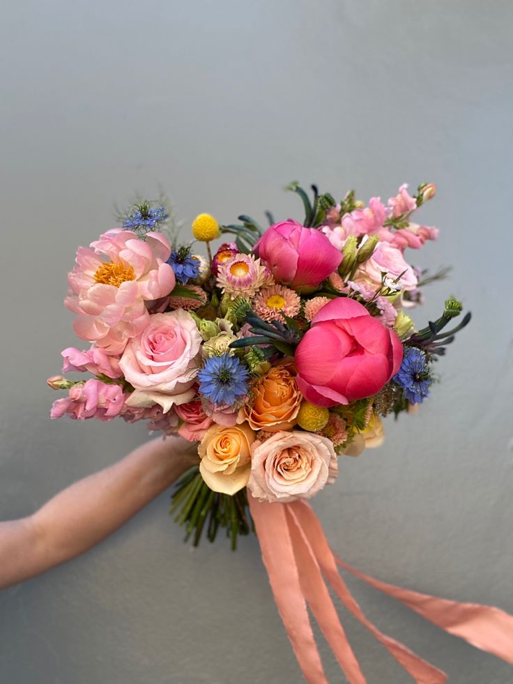 a bridal bouquet with pink, orange and blue flowers is held by a woman's hand