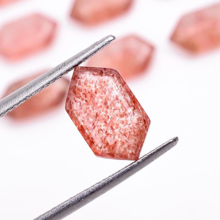 a pink diamond being held by two metal tongs with other diamonds in the background