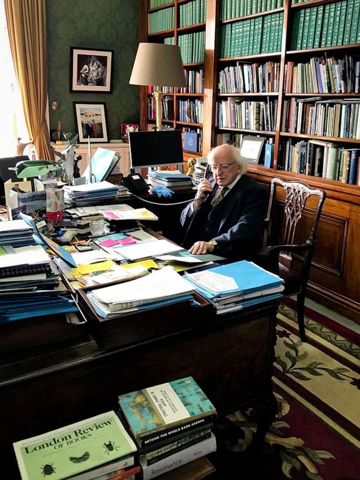 an older man sitting at a desk with many books on it