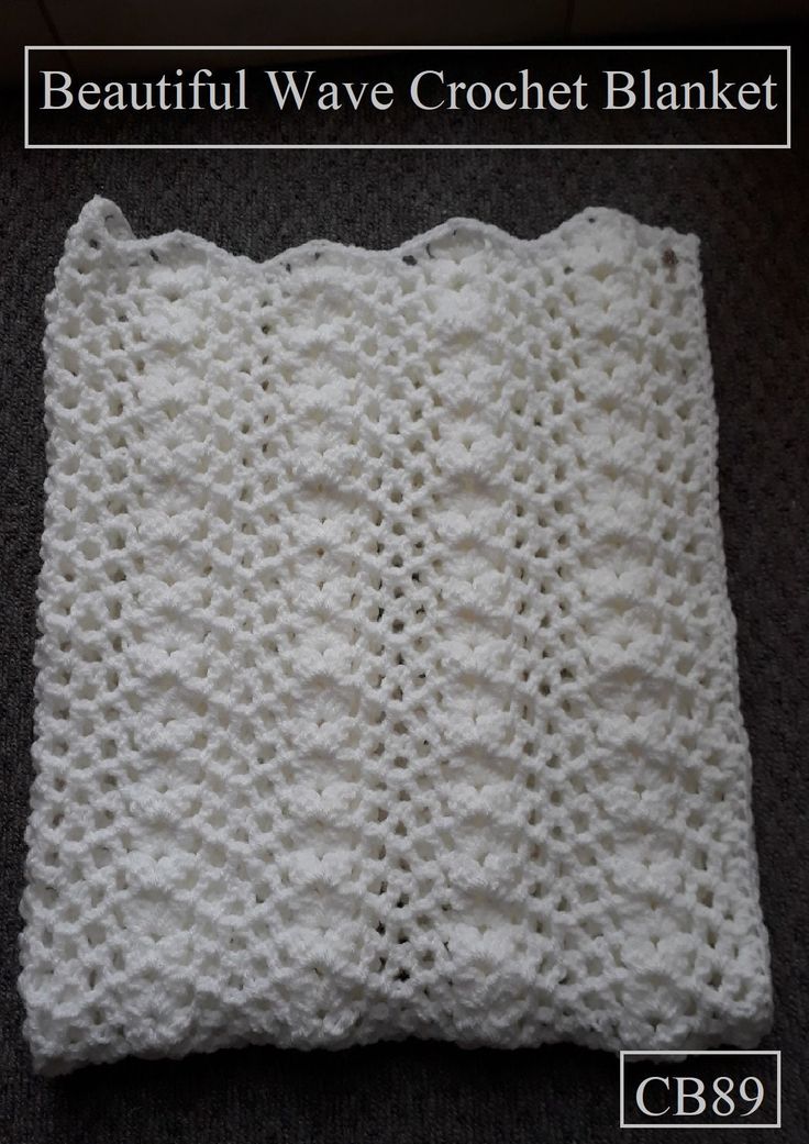 a white crochet blanket sitting on top of a black floor next to a pillow