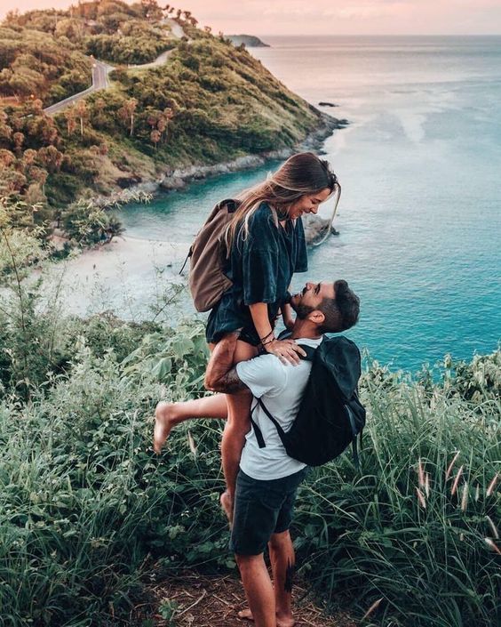 a man carrying a woman on his back while standing next to the ocean