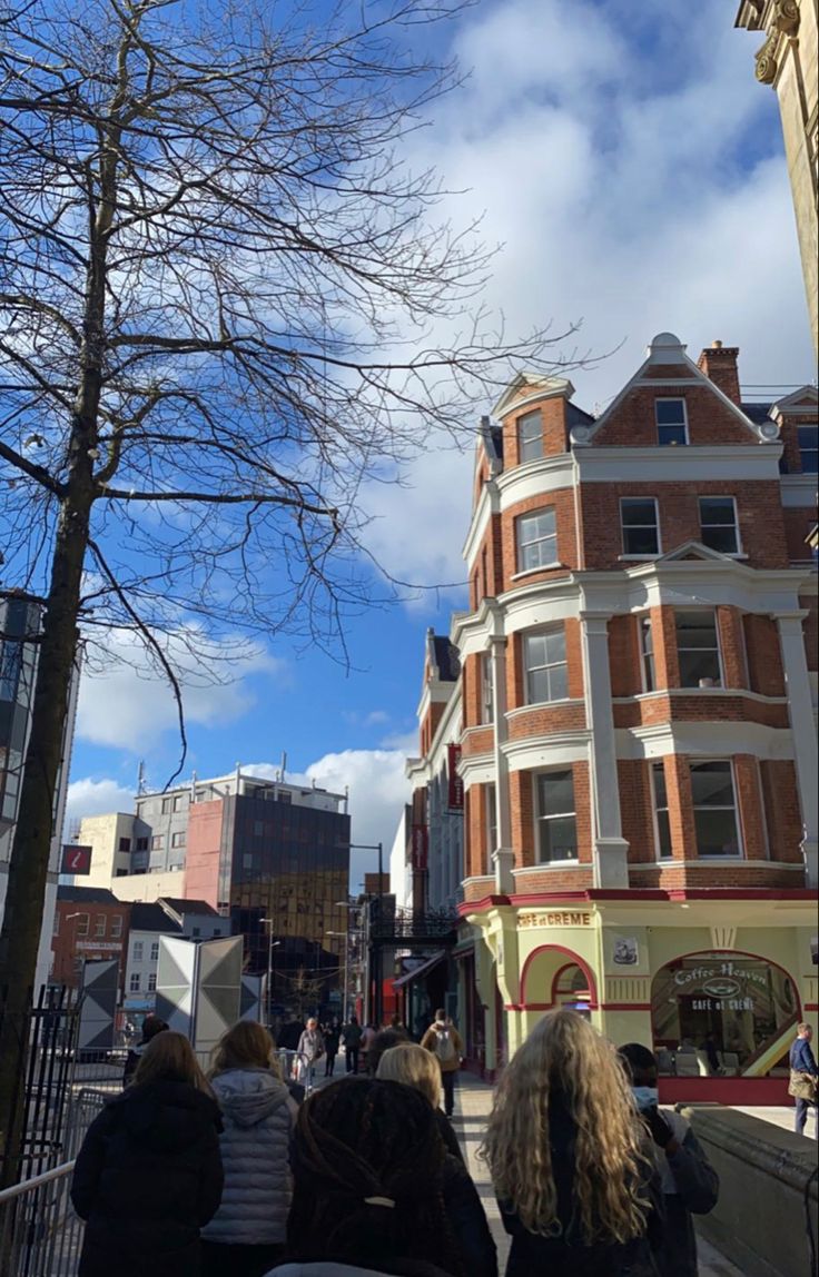 several people are walking down the street in front of some buildings and trees with no leaves on them