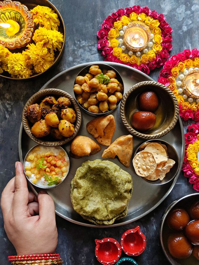 a person holding a plate full of food on a table with flowers and candles around it