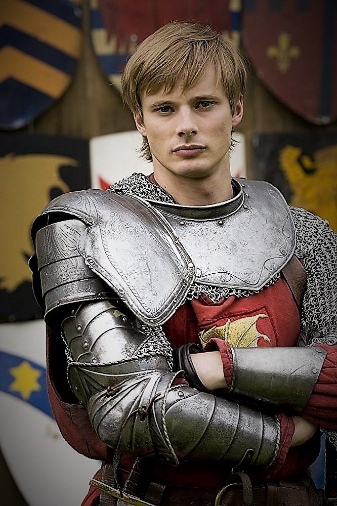 a young man dressed as a knight with his arms crossed and wearing armor, standing in front of shields