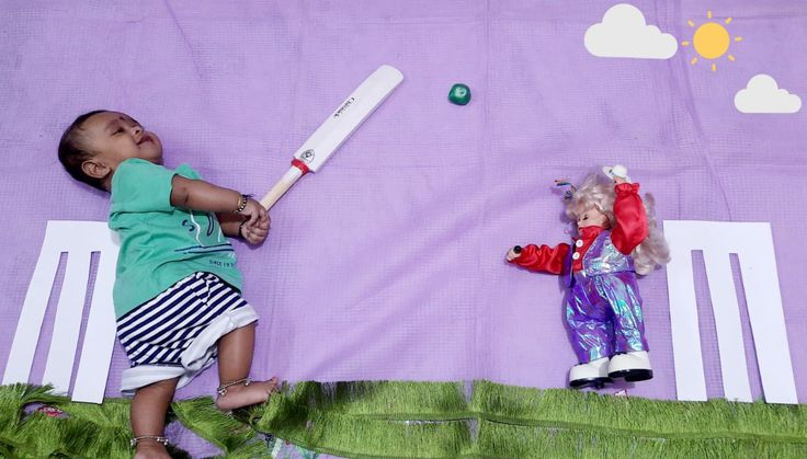 two dolls laying on top of a bed next to a purple blanket with green grass