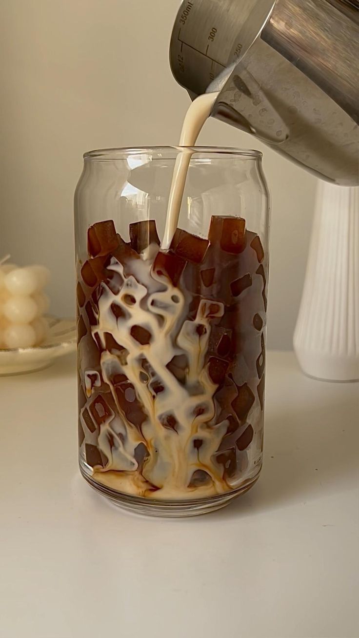 a person pouring something into a glass with ice cream and toppings in it on a table