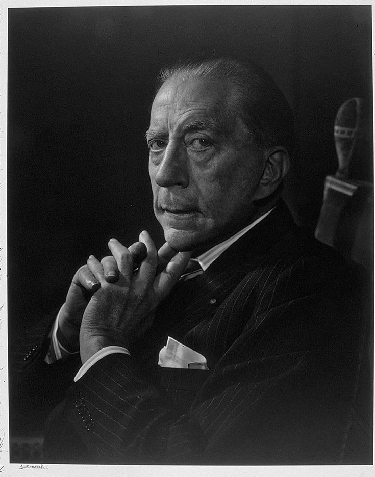 a black and white photo of a man with his hands clasped in front of him