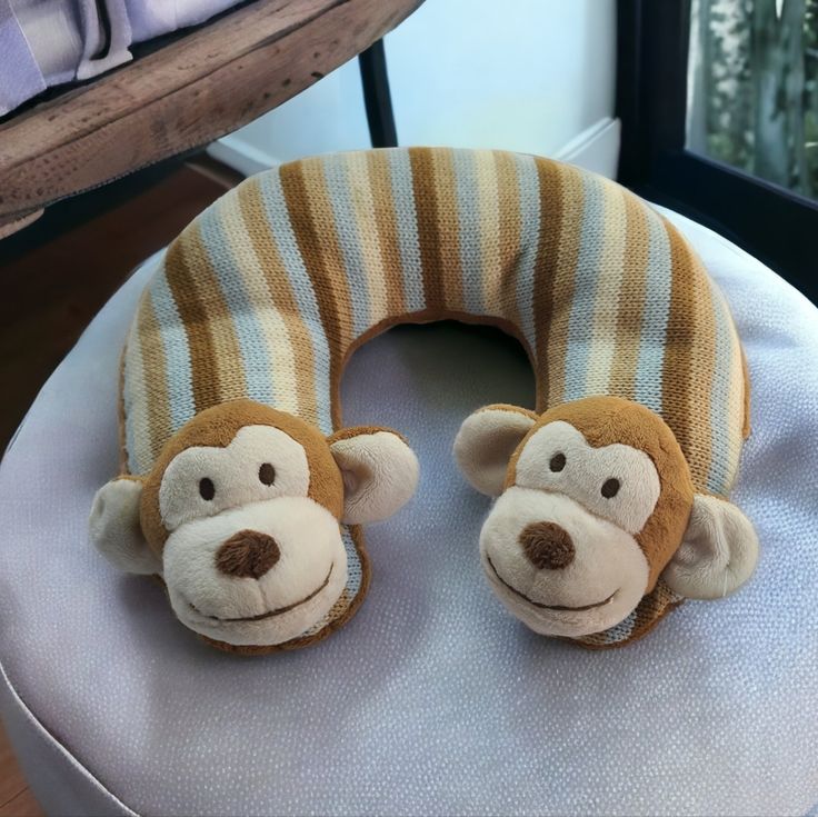 two stuffed monkeys sitting on top of a white chair next to a pillow that is shaped like a monkey