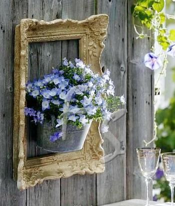 blue flowers are in a bucket hanging on a wooden wall next to two wine glasses