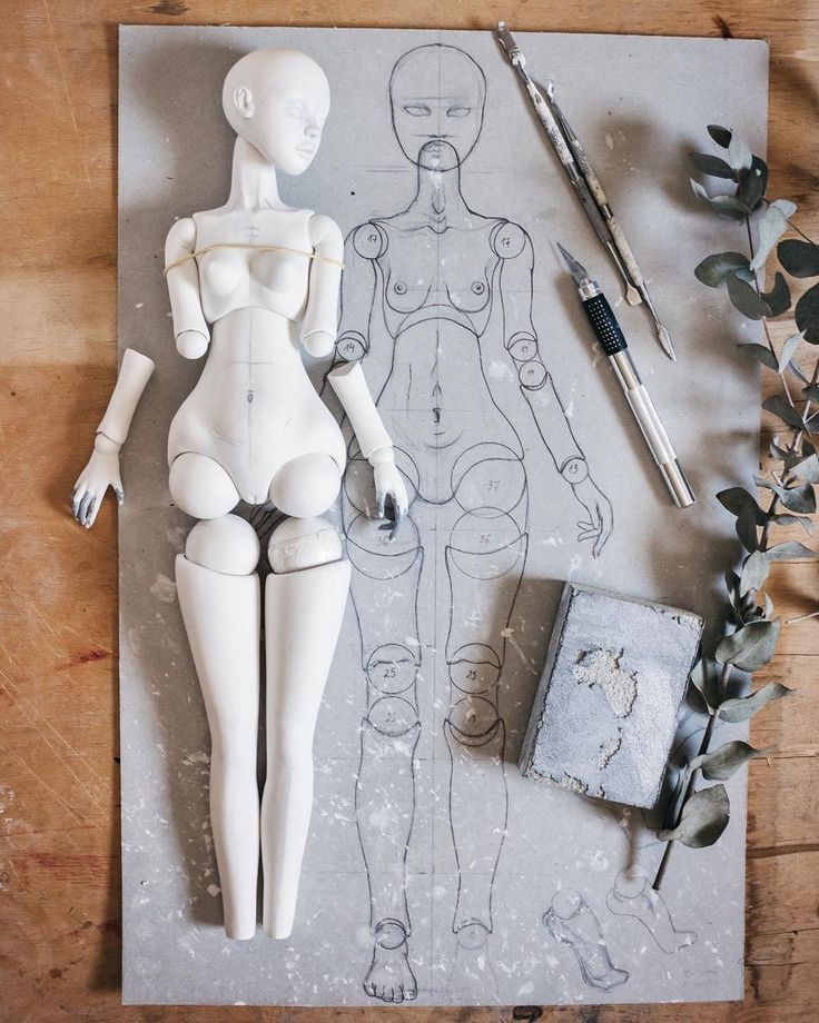 a white mannequin sitting on top of a piece of paper next to a plant