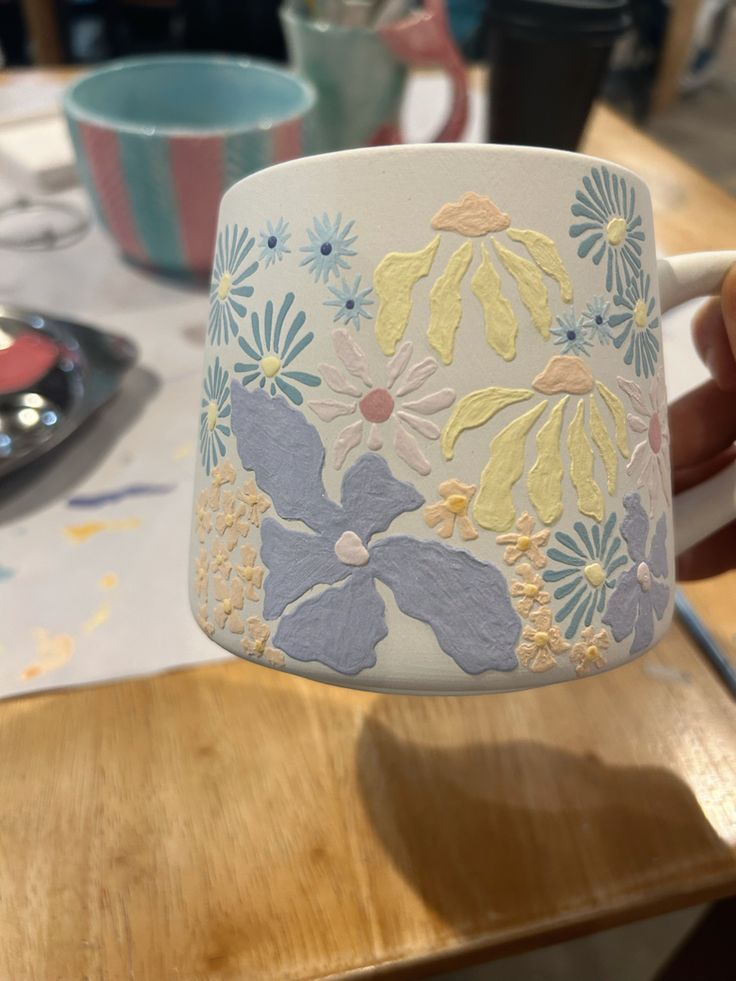 a person holding up a coffee cup with flowers on the inside and outside, while sitting at a table