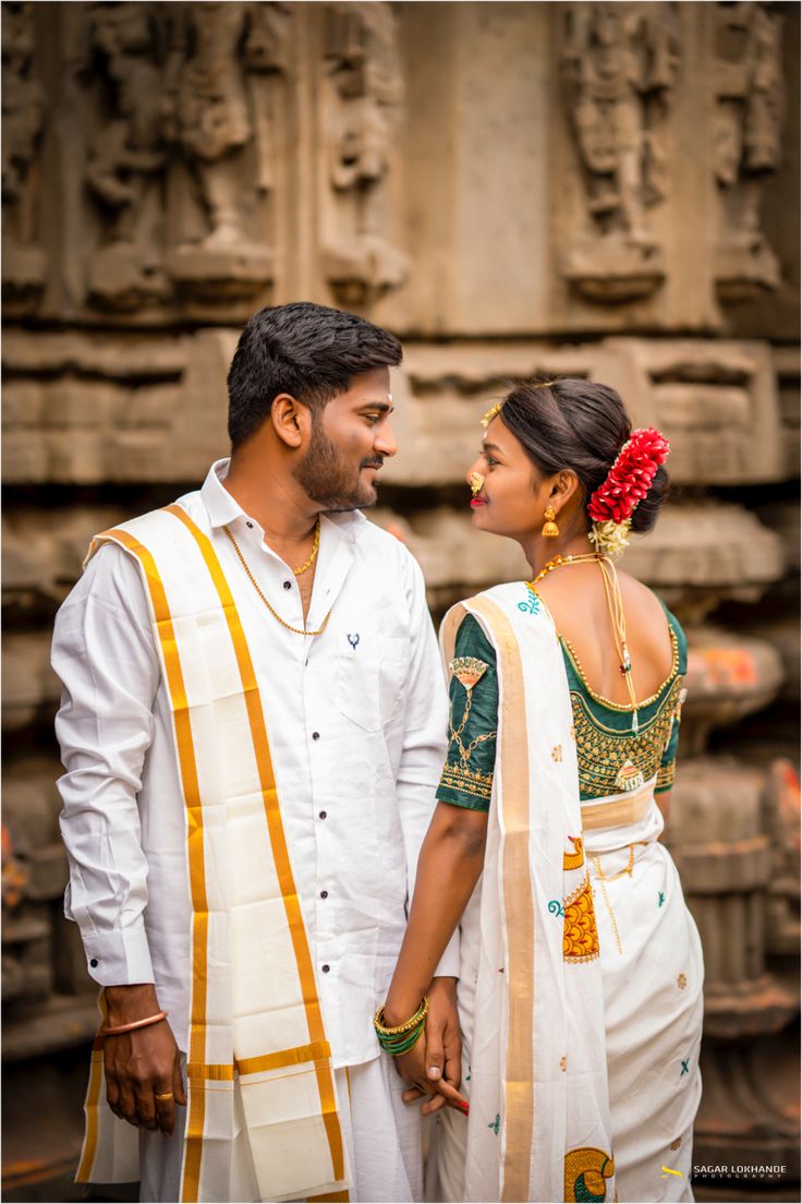 a man and woman standing next to each other in front of a stone wall with carvings on it