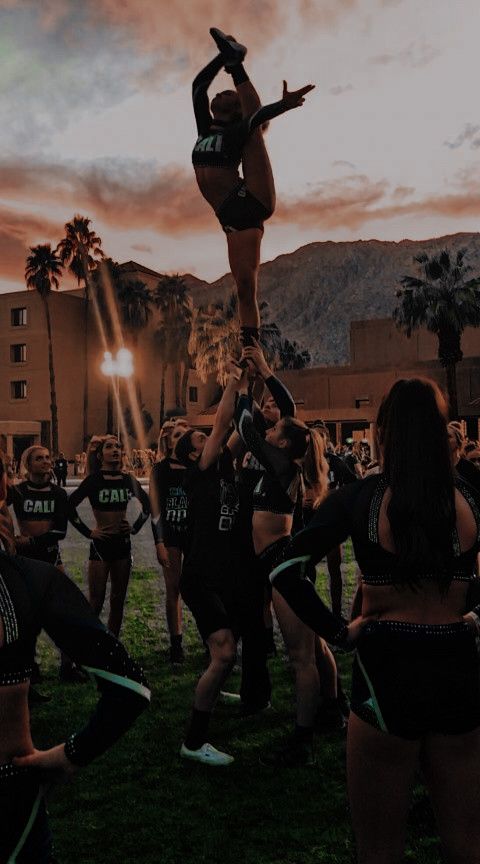 a group of cheerleaders standing around each other in front of a red sky