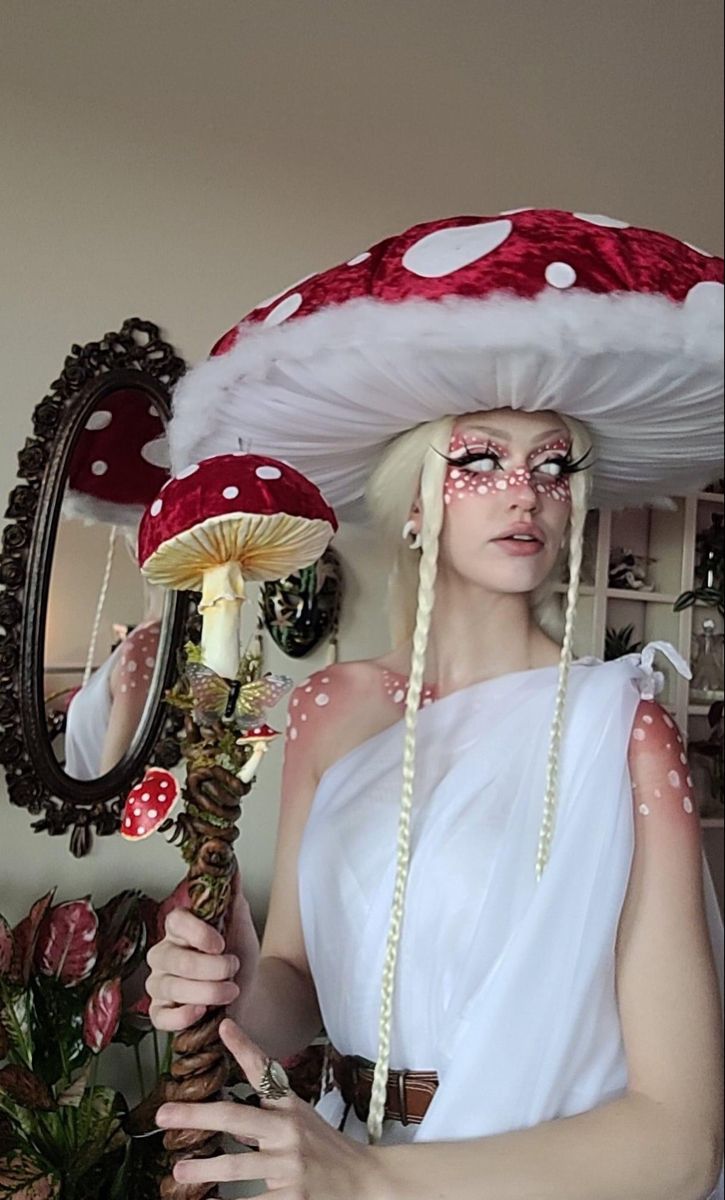 a woman in white dress and red mushroom hat holding up a mirror to her face