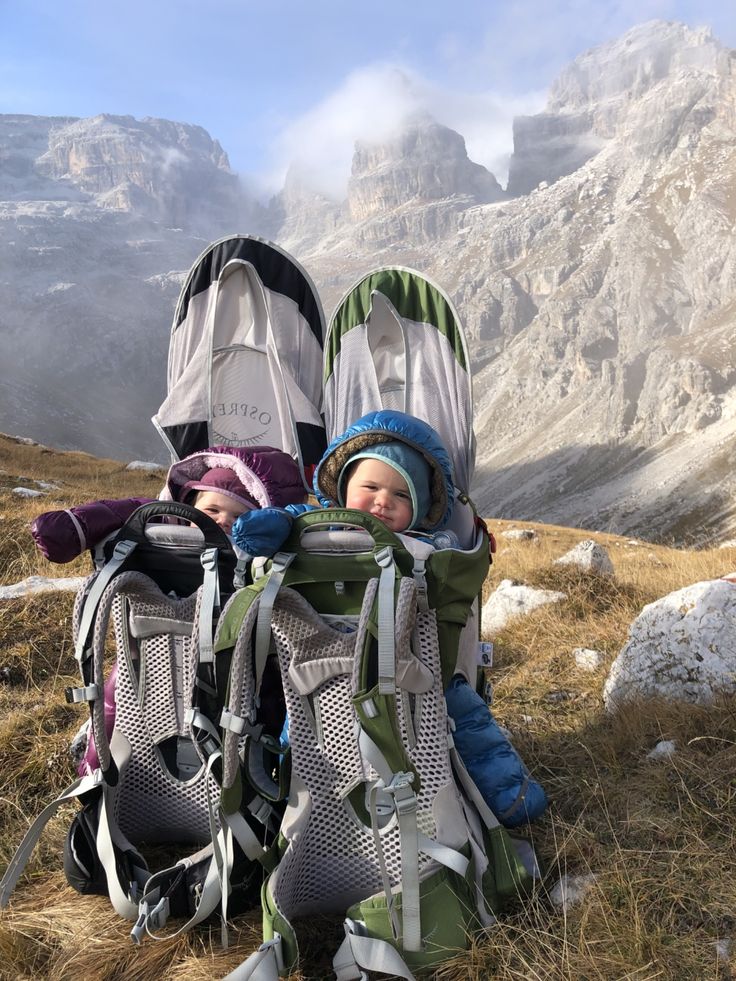 two children sitting in backpacks on the side of a mountain