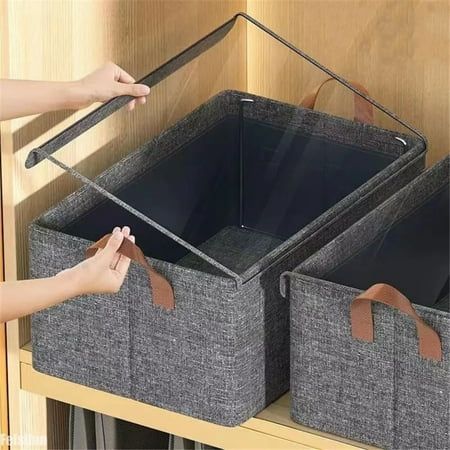 two gray baskets with brown handles are on a wooden shelf and someone is reaching for them