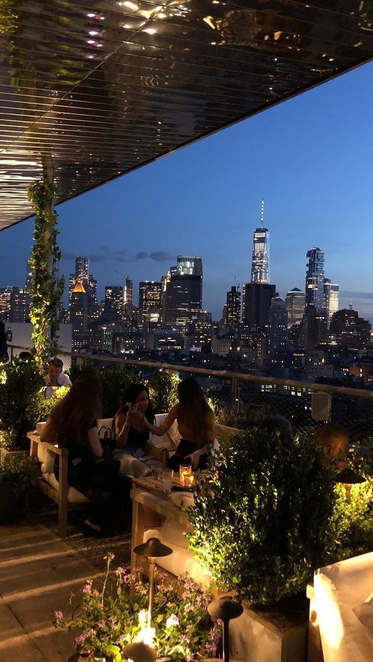 people sitting at tables on top of a roof with the city skyline in the background