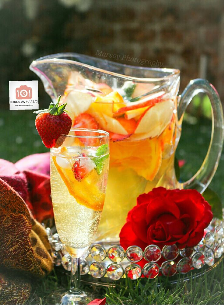 a pitcher filled with liquid next to a glass full of ice and strawberries on the grass