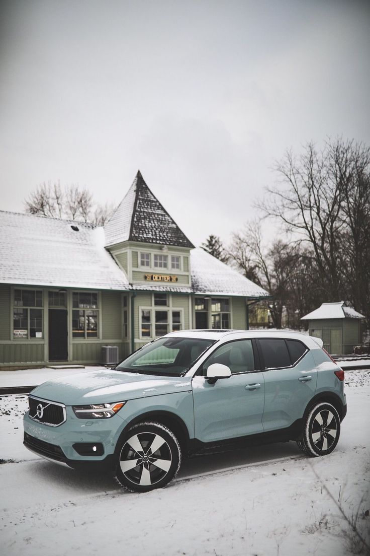 a light blue car parked in front of a building with snow on the ground and trees