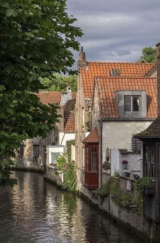 a river running through a small town next to tall buildings with red roof tops on either side