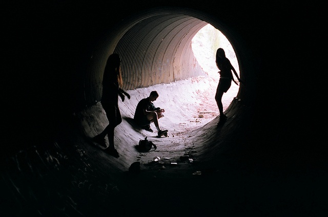 three people are standing in a dark tunnel with snow on the ground and one person is kneeling down