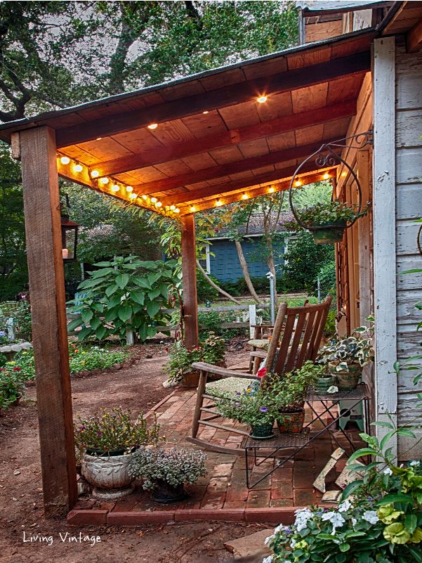 an outdoor covered patio with chairs and string lights on the roof, surrounded by greenery