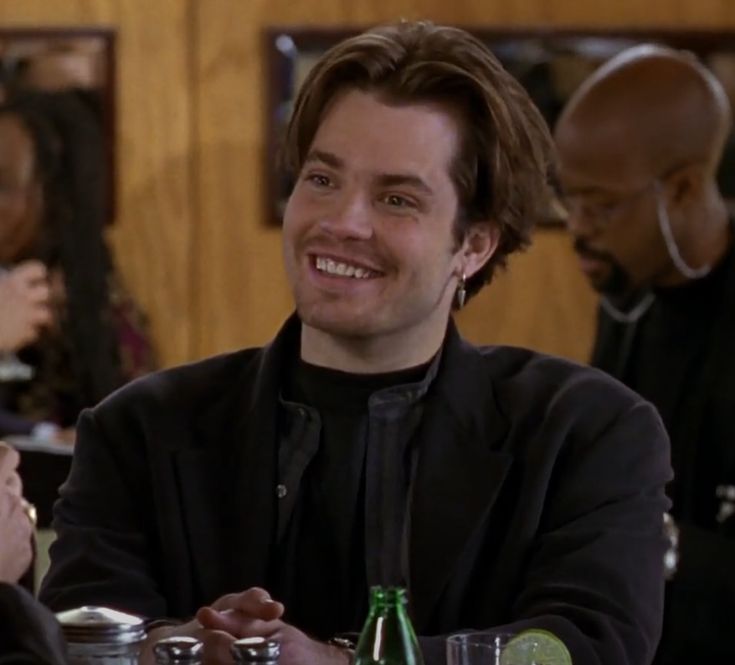 a man sitting at a table smiling for the camera with other people in the background