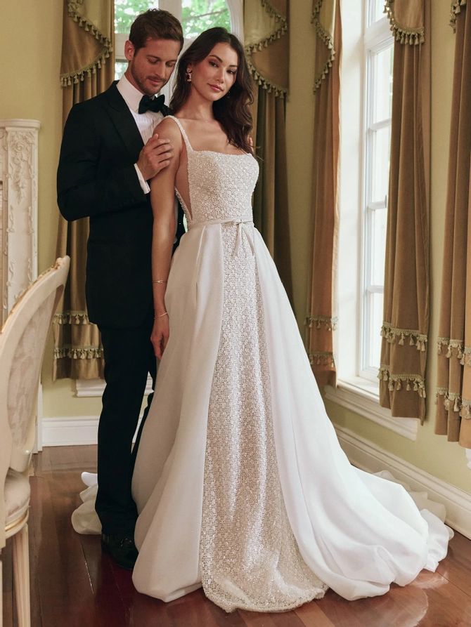 a man and woman standing next to each other in front of a window wearing wedding gowns