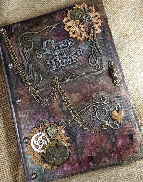 an altered book with gears and chains on the cover is sitting on a piece of fabric