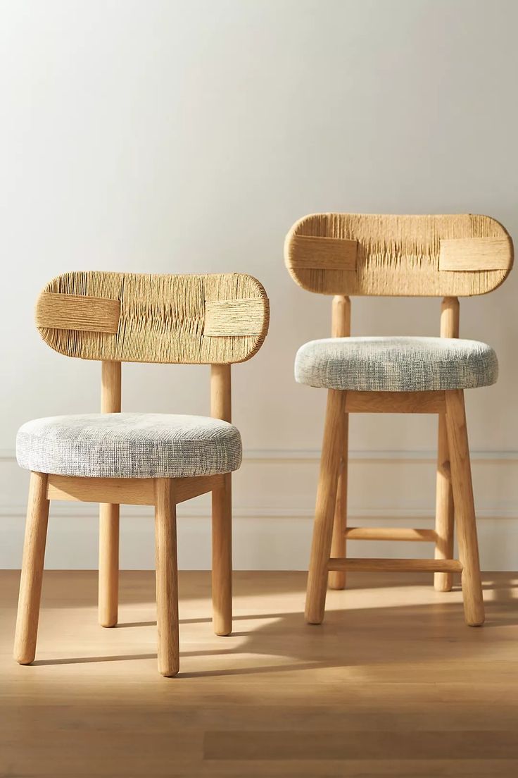 two wooden chairs sitting next to each other on top of a hard wood floor in front of a white wall