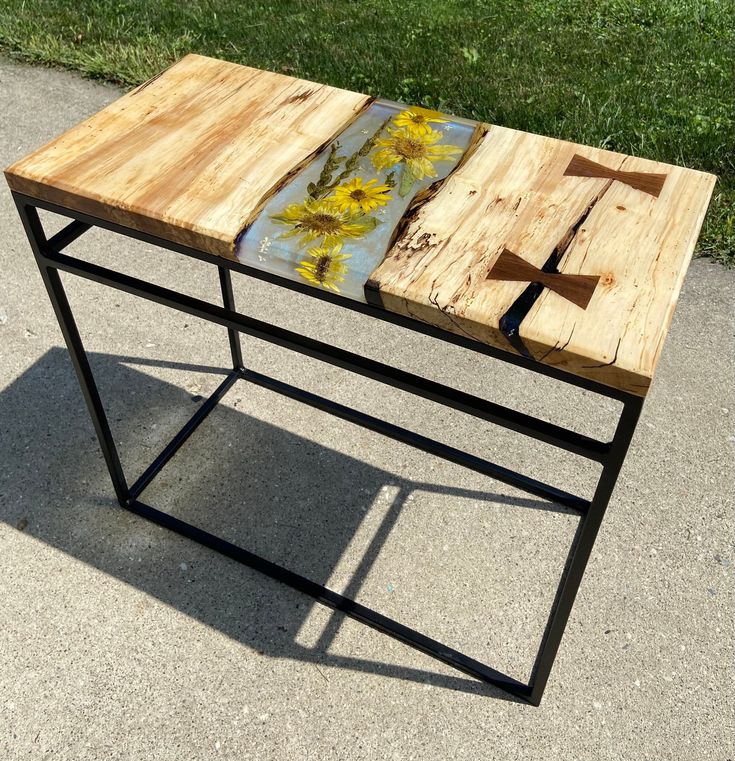 a table made out of wood and metal with yellow flowers painted on it, sitting in the middle of a sidewalk